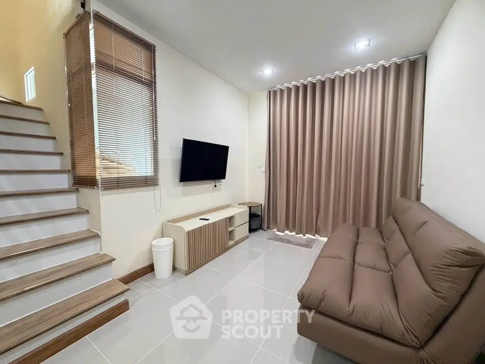 Modern living room with sleek design, featuring a cozy sofa, wall-mounted TV, and elegant staircase.