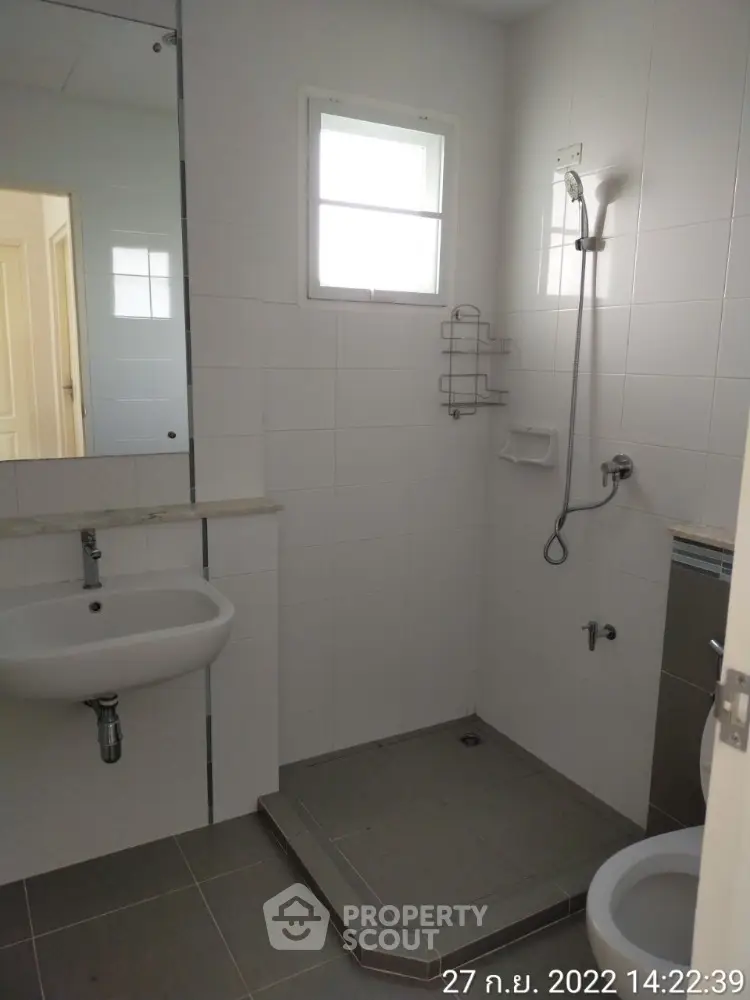 Pristine white-tiled bathroom featuring a walk-in shower, pedestal sink, and a large mirror reflecting a bright interior.