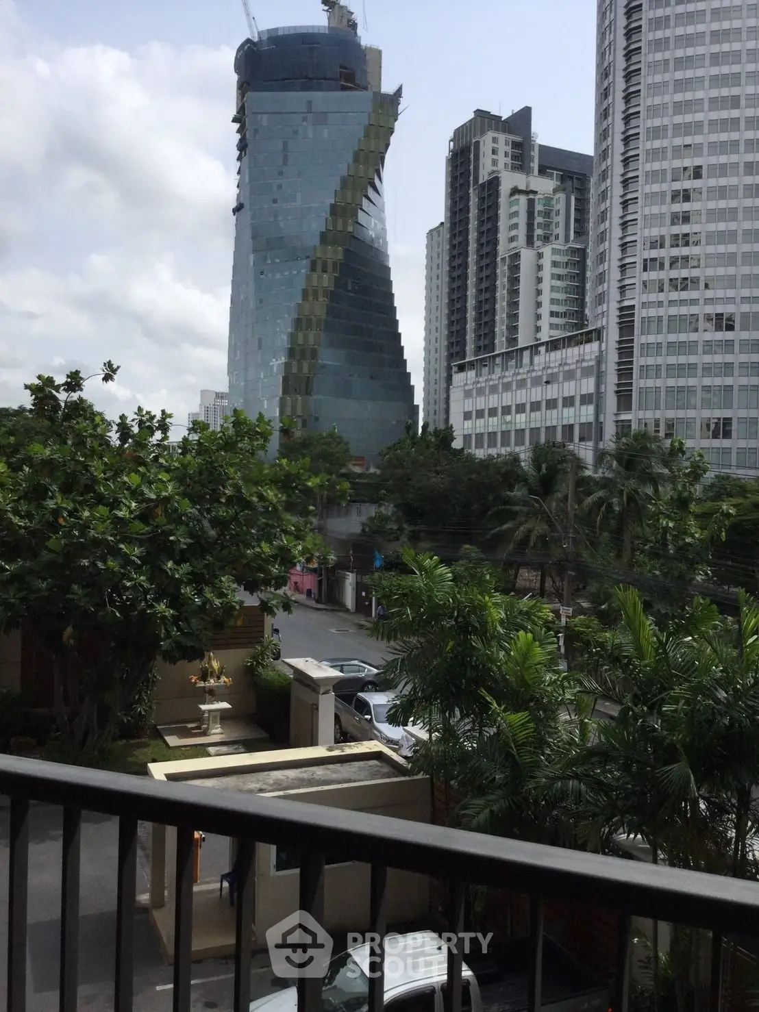 Stunning cityscape view from a balcony overlooking modern skyscrapers and lush greenery.