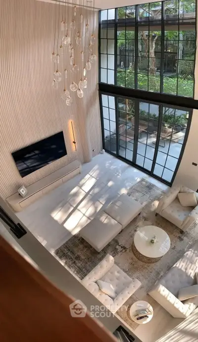 Luxurious modern living room with high ceilings, elegant chandelier, and large windows overlooking a garden.