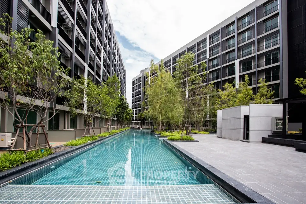 Modern apartment complex with a central swimming pool and lush greenery.