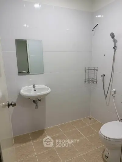 Modern bathroom with sleek white tiles and minimalist fixtures, featuring a wall-mounted sink and shower area.