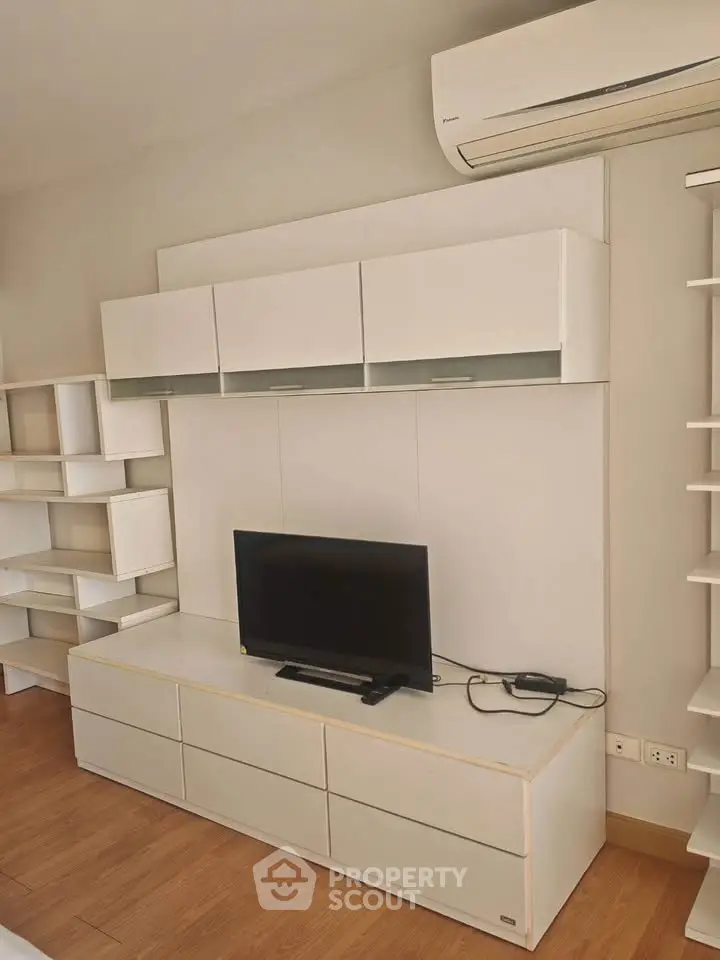 Modern living room with sleek white cabinetry and mounted TV, featuring a minimalist design and air conditioning.