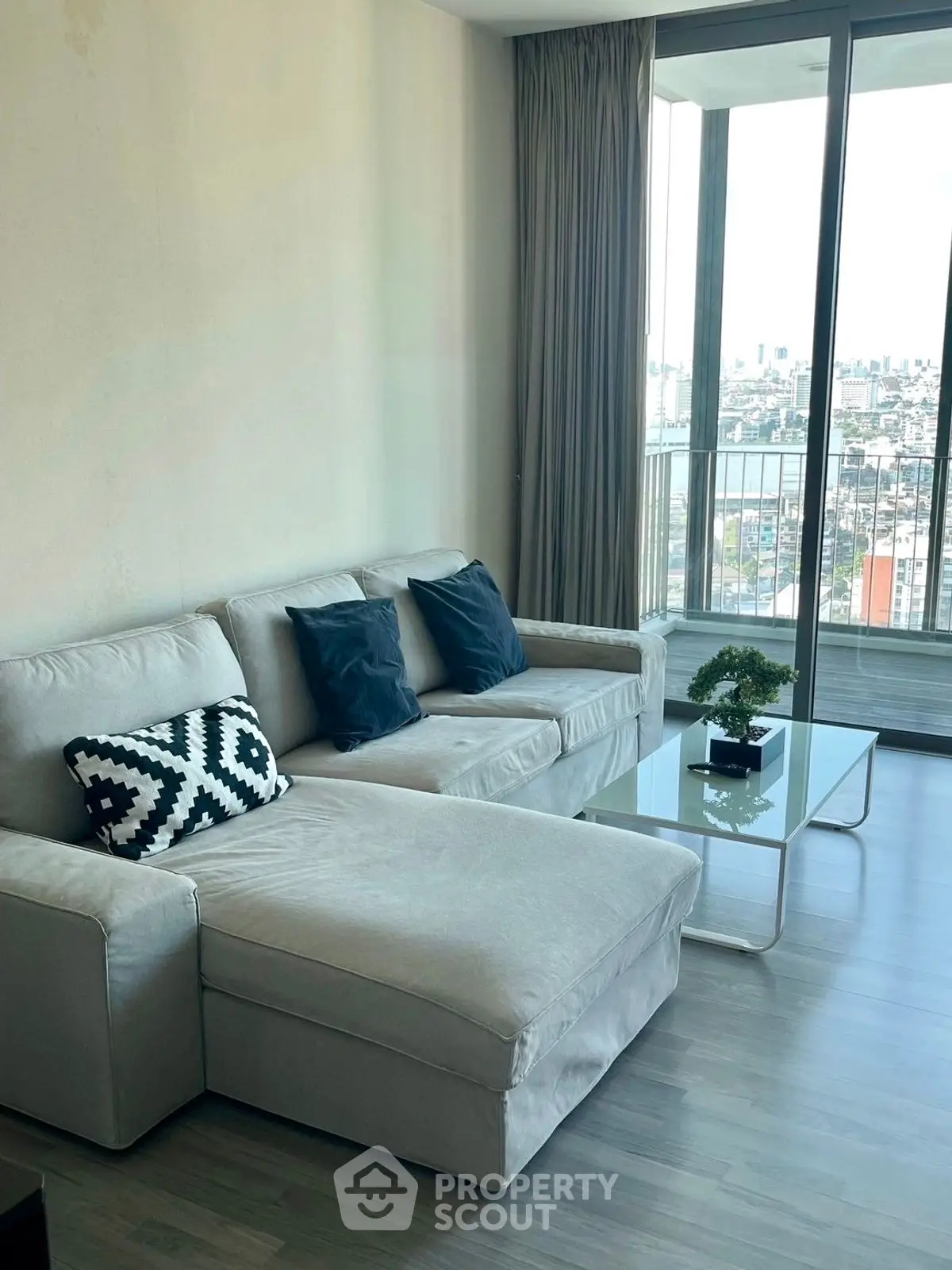 Modern living room with large windows and city view, featuring a stylish sofa and glass coffee table.