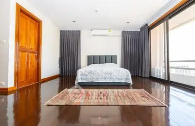 Spacious bedroom with wooden flooring and large windows offering natural light.