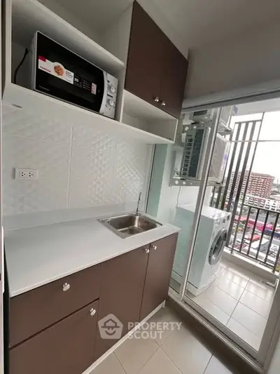 Modern compact kitchen with microwave and washing machine, city view from balcony.