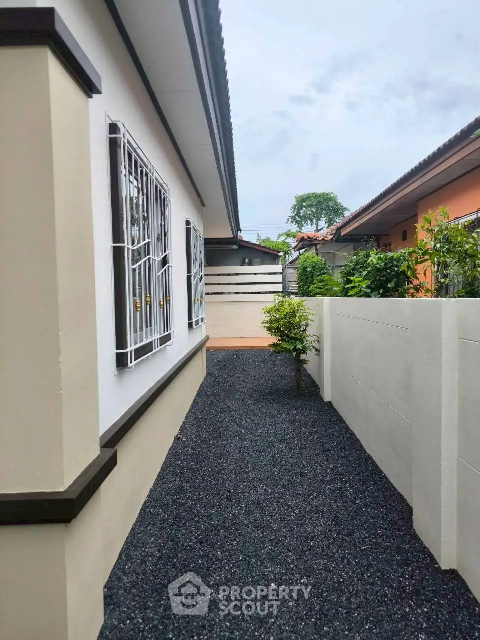 Charming exterior view of a single-story home with a neat side pathway and lush greenery.