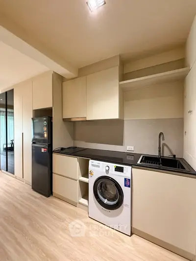 Modern kitchen with sleek cabinetry, built-in washing machine, and compact fridge in a stylish apartment.