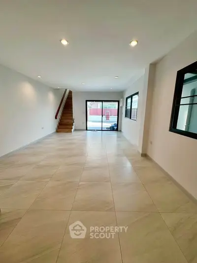 Spacious modern living room with elegant staircase and large windows for natural light.