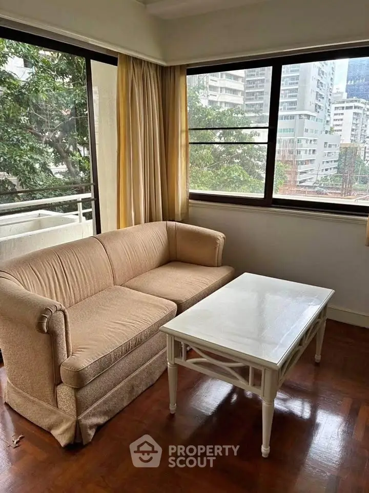 Cozy living room with beige sofa and white coffee table, large windows with city view.