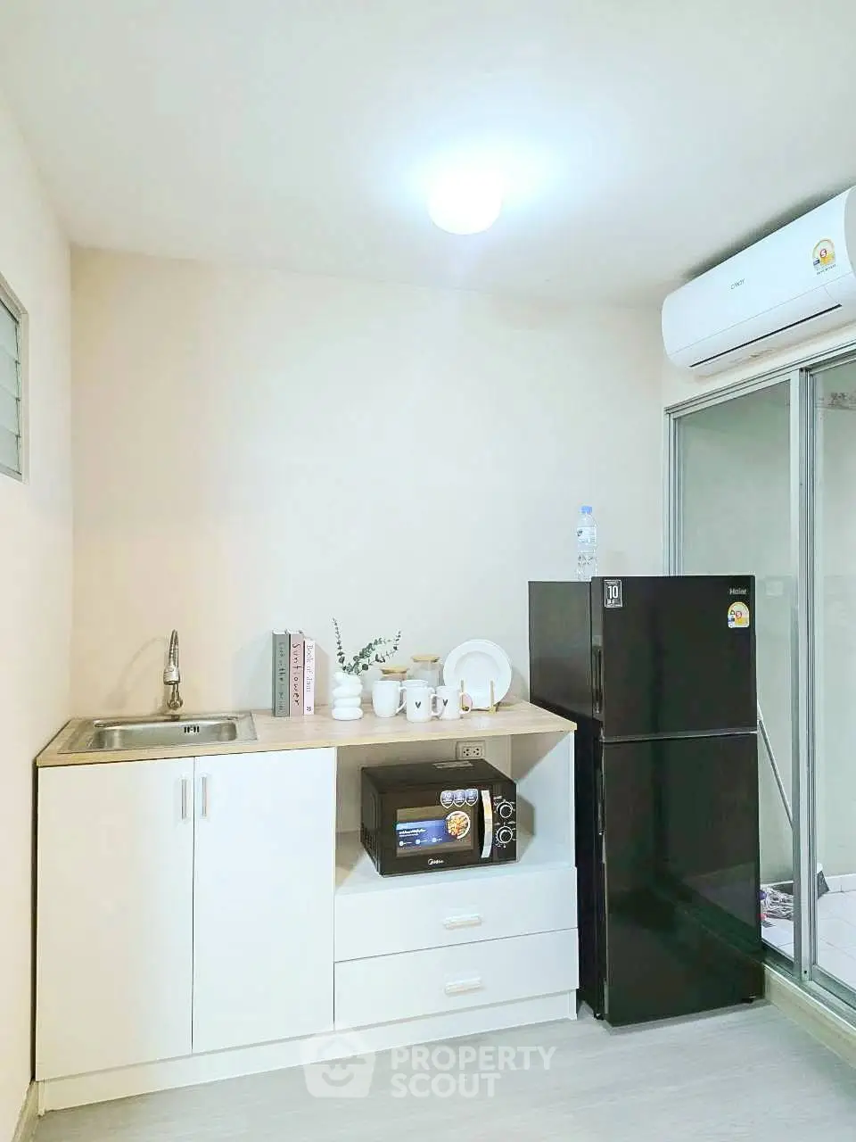 Modern kitchen with sleek black fridge and compact white cabinetry, featuring a microwave and stylish decor.