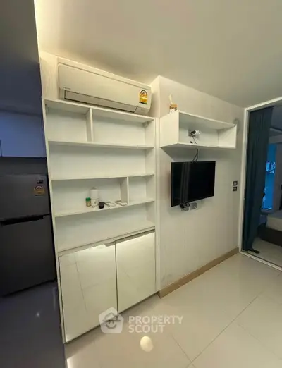 Modern living room with sleek white shelving and wall-mounted TV, adjacent to a cozy bedroom.