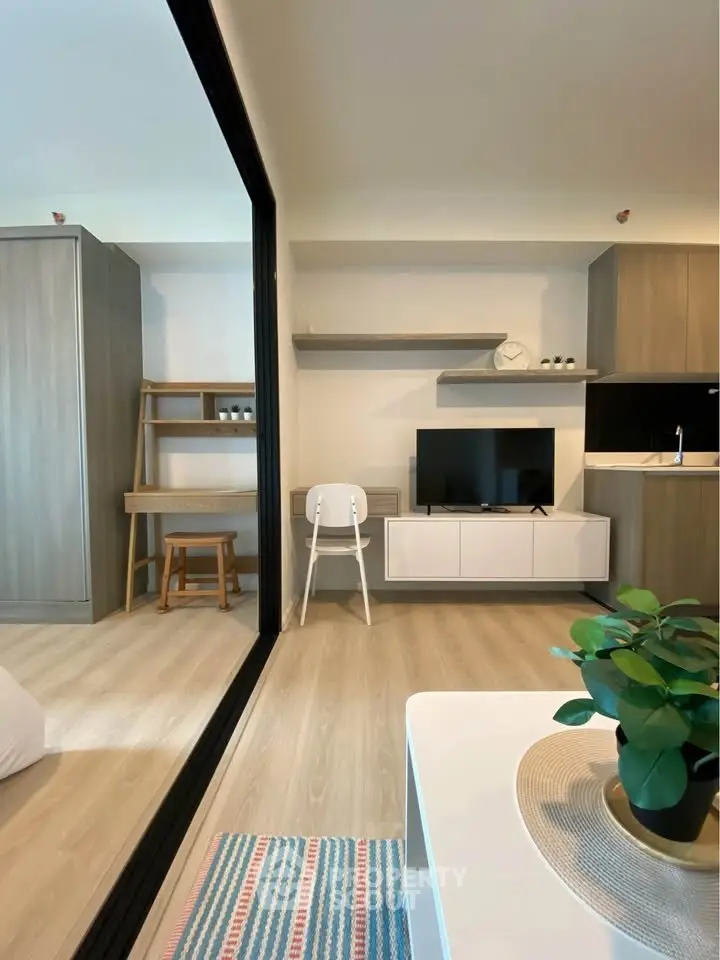 Modern living room with stylish decor and open layout, featuring a TV, shelving, and a cozy workspace.