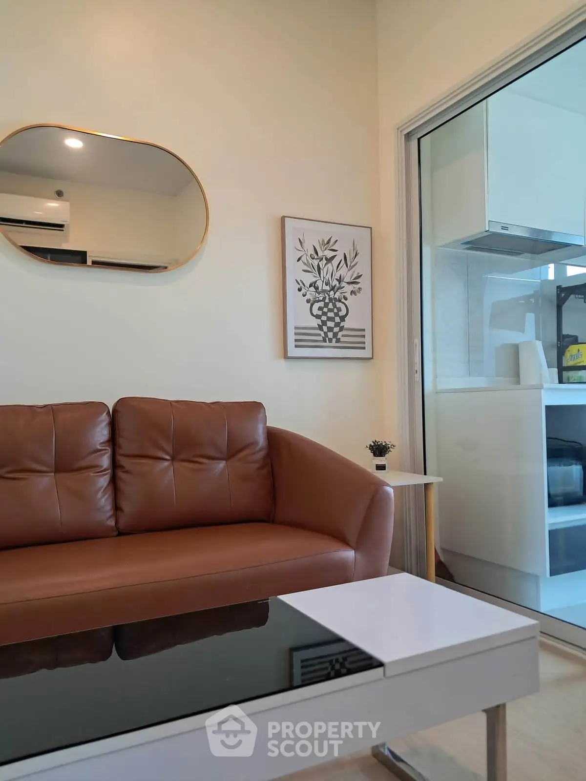 Modern living room with brown leather sofa and stylish decor adjacent to a sleek kitchen area.