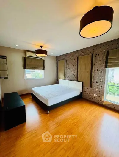 Spacious bedroom with modern decor and wooden flooring, featuring large windows for natural light.