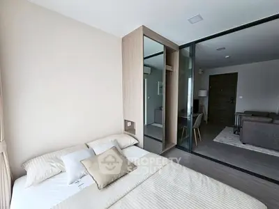 Modern bedroom with sliding glass doors leading to a cozy living area, featuring neutral tones and stylish decor.