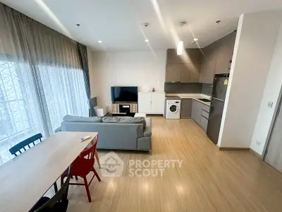 Modern open-plan living room with kitchen and dining area, featuring sleek furniture and natural light.