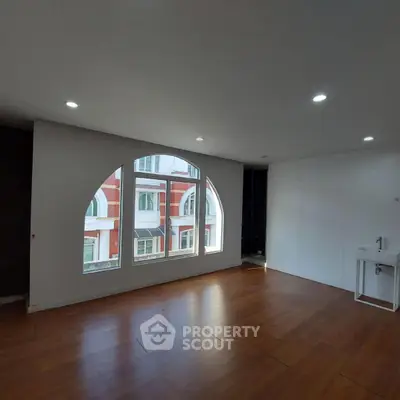 Spacious room with large arched window and wooden flooring