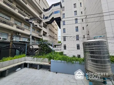 Urban rooftop view with water tank and greenery, surrounded by modern buildings.