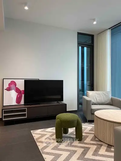 Modern living room with stylish furniture and large TV, featuring contemporary art and natural light.