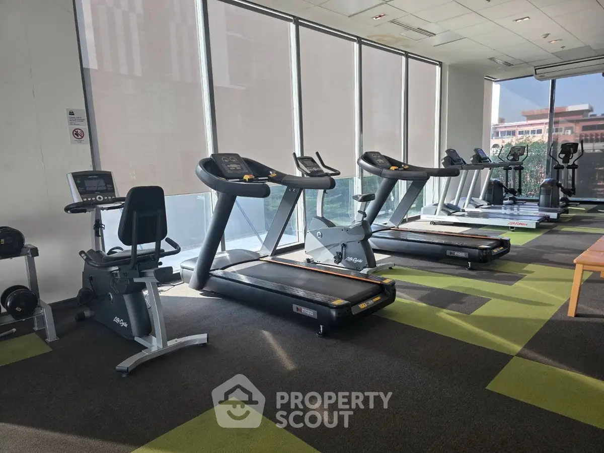 Modern gym with treadmills and exercise equipment in a bright, spacious area with large windows.