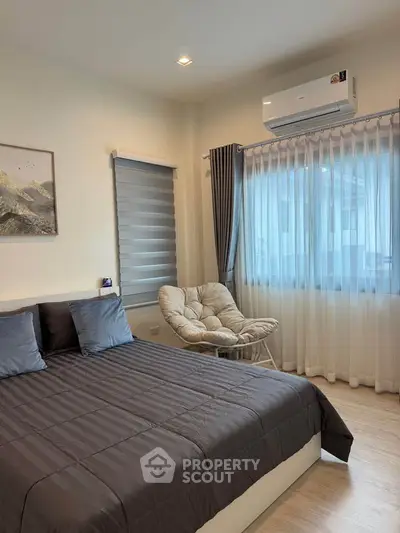 Cozy bedroom with modern decor, featuring a comfortable bed, stylish chair, and air conditioning.