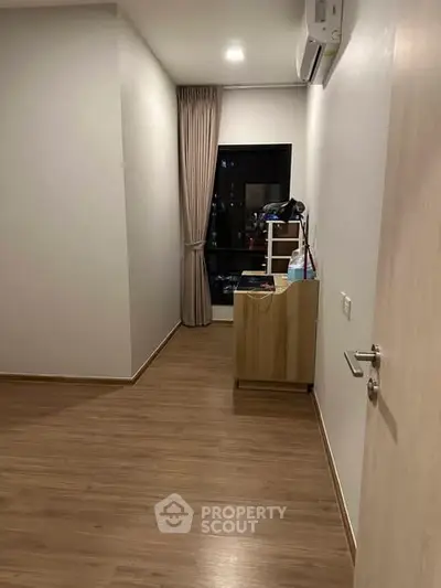 Spacious empty room with wooden flooring and large window, ideal for customization.