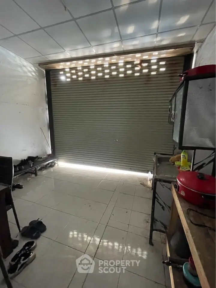Spacious storage room with tiled floor and metal shutter door, ideal for versatile use.