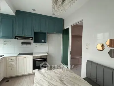 Modern kitchen with teal cabinets, marble table, and built-in oven in stylish apartment.