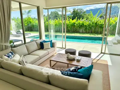 Luxurious living room with pool view and lush greenery, featuring elegant sofas and modern decor.