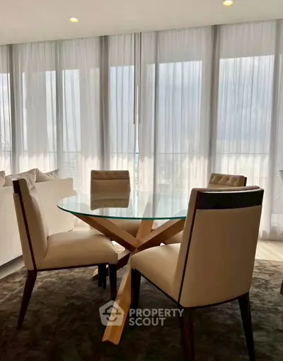 Elegant dining area with glass table and plush chairs in a modern apartment with floor-to-ceiling windows.