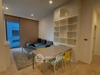 Modern living room with sleek furniture and built-in shelving, featuring a cozy dining area and balcony access.