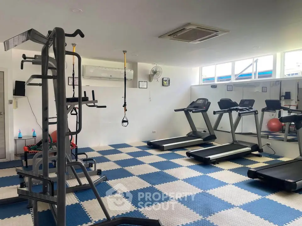 Spacious gym with modern equipment and bright natural lighting in a residential building.