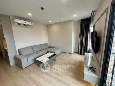 Modern living room with sleek furniture and large window offering city views.