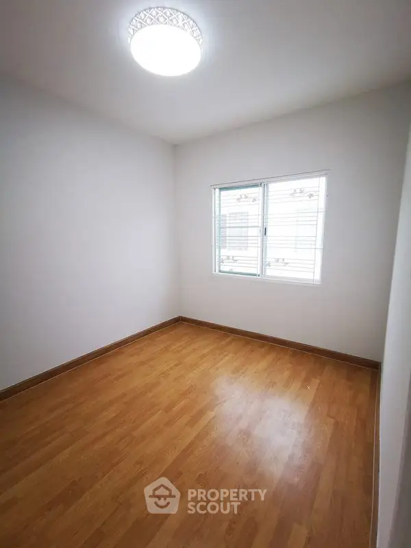 Spacious empty room with wooden flooring and bright window