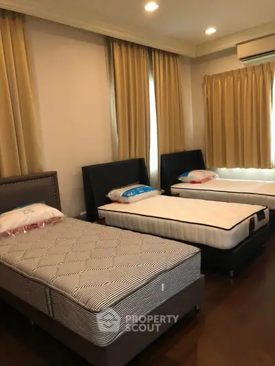 Spacious bedroom with three single beds and elegant curtains, perfect for shared living.