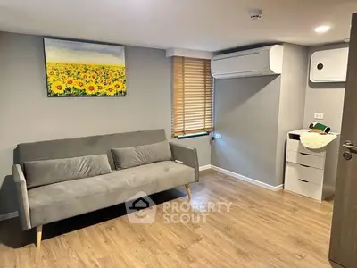 Modern living room with gray sofa, wooden floor, and air conditioning unit.