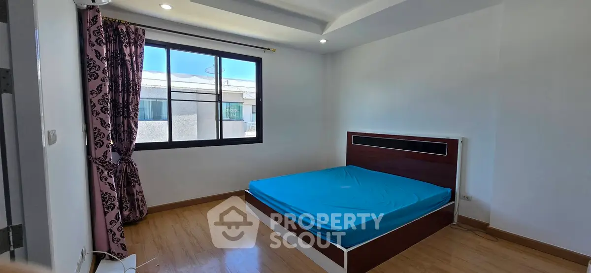 Spacious bedroom with large window and modern bed frame, offering natural light and comfort.