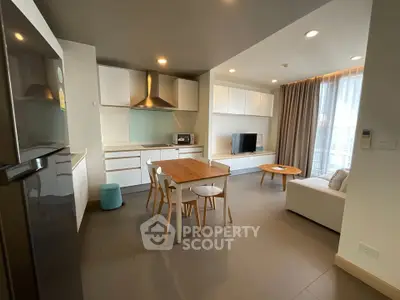 Modern open-layout living room with kitchen and dining area, featuring sleek furniture and natural light.