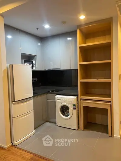 Modern kitchen with sleek cabinetry, washing machine, and fridge in compact layout.