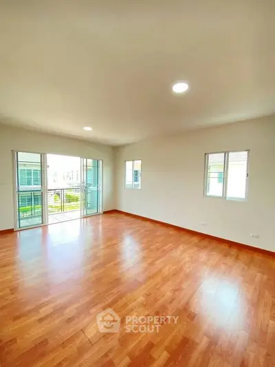 Spacious empty room with wooden flooring and large windows in a modern home.