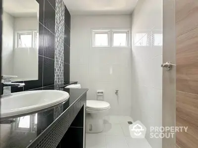 Modern bathroom with sleek black and white tiles, featuring a stylish sink and toilet.