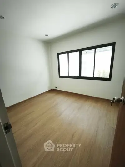 Spacious empty room with wooden flooring and large window, perfect for customization.
