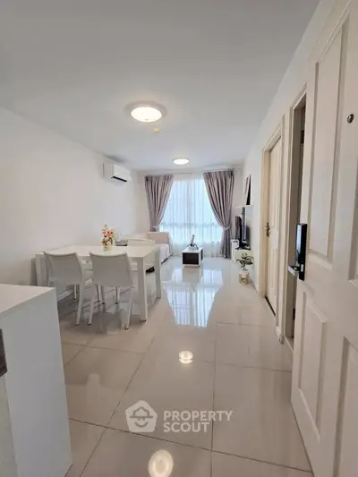 Modern open-plan living room with dining area, featuring sleek white furniture and large windows for natural light.