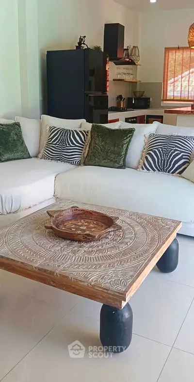 Stylish living room with modern decor and open kitchen layout, featuring a unique carved wooden coffee table.