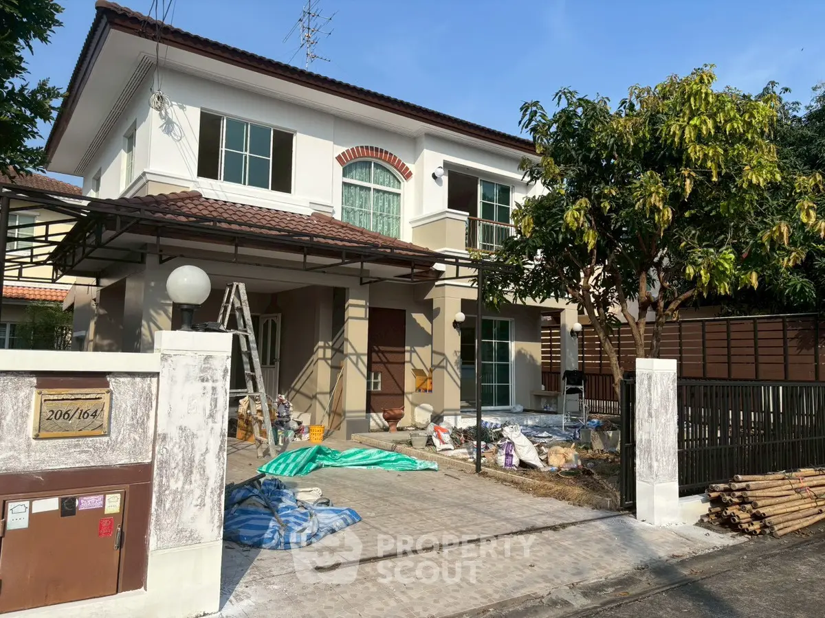 Charming two-story house with modern exterior under renovation, featuring a spacious driveway and lush greenery.