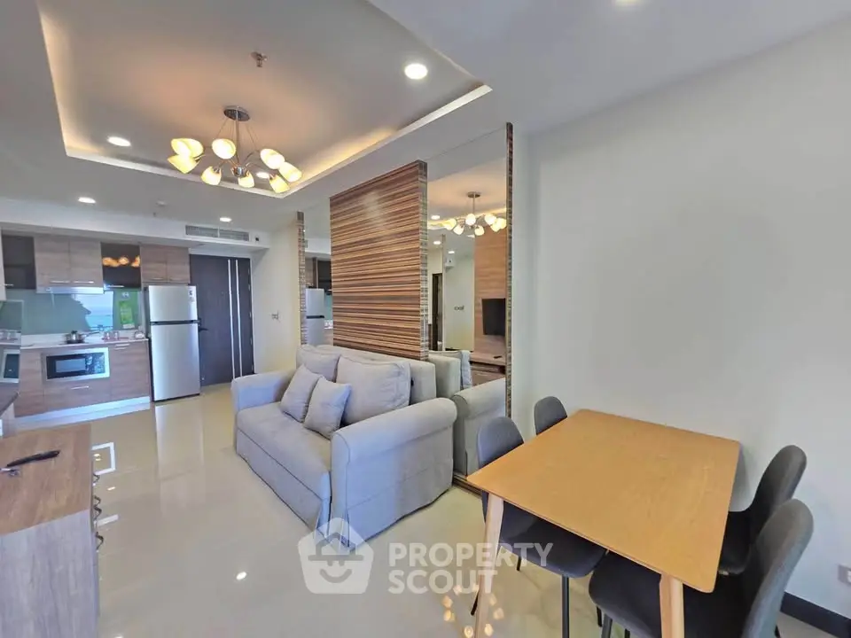 Modern open-plan living room with stylish kitchen and dining area, featuring contemporary lighting and sleek furniture.