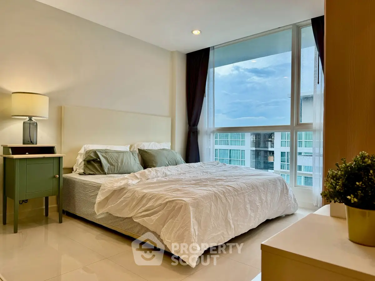Modern bedroom with large window offering city view, featuring cozy bed and stylish decor.