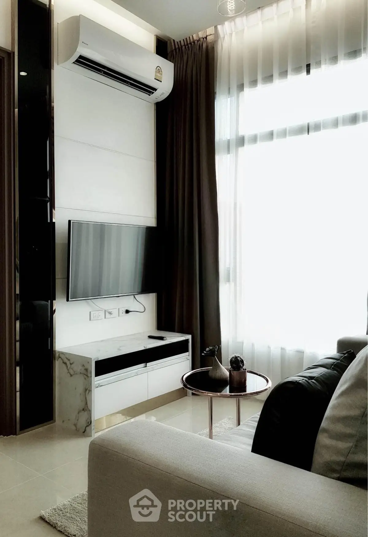 Modern living room with sleek furniture and natural light, featuring a wall-mounted TV and air conditioning.