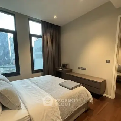 Modern bedroom with city view, featuring elegant decor and large windows for natural light.